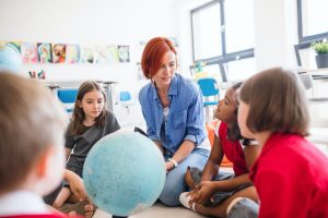 A group of small school kids with teacher sitting on the floor in class, learning