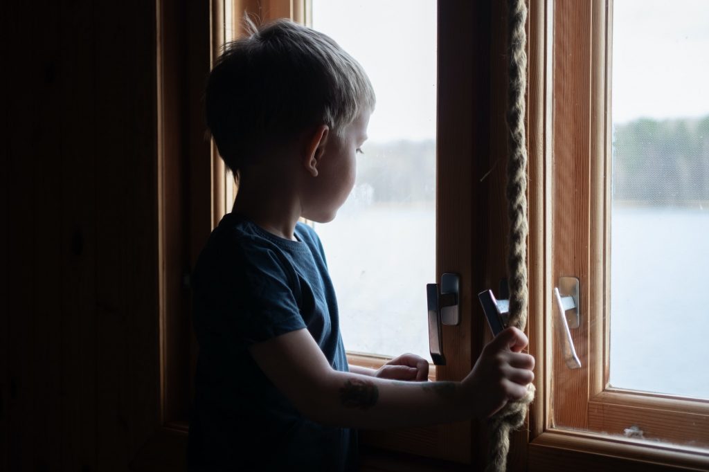 Little boy silhouette near the window looking outside. Depression; lockdown; self isolation; social