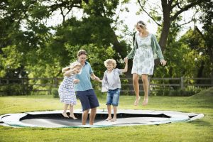 Man, woman, boy and girl holding hands, jumping on a trampoline set into the ground in a garden.
