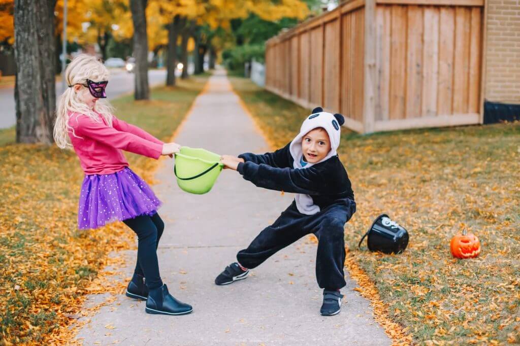 Friends children fighting for basket after Halloween celebration trick or treat. Siblings quarrel.