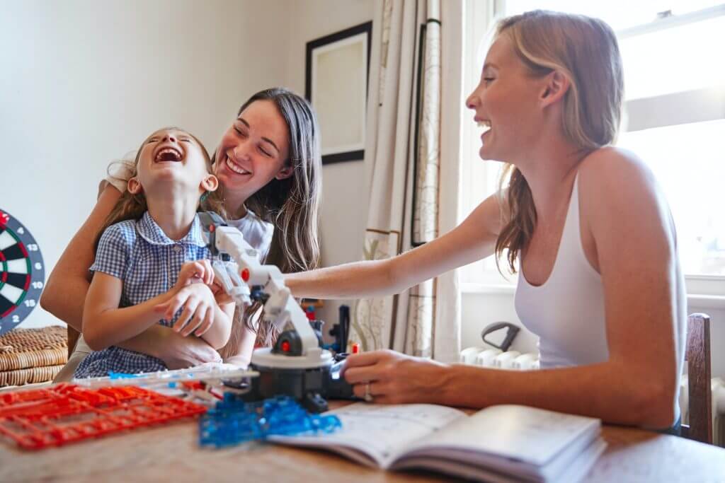Same Sex Female Couple Making Robot From Kit With Daughter In Bedroom At Home Together