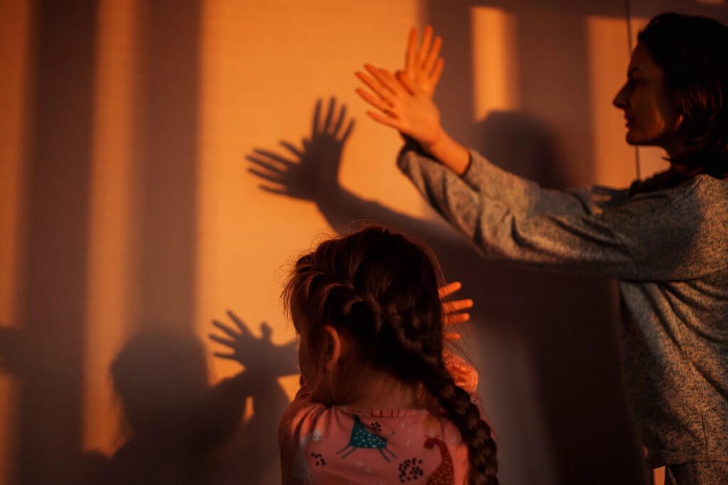 Mom and daughter play shadow theater on the wall in the light of the setting sun